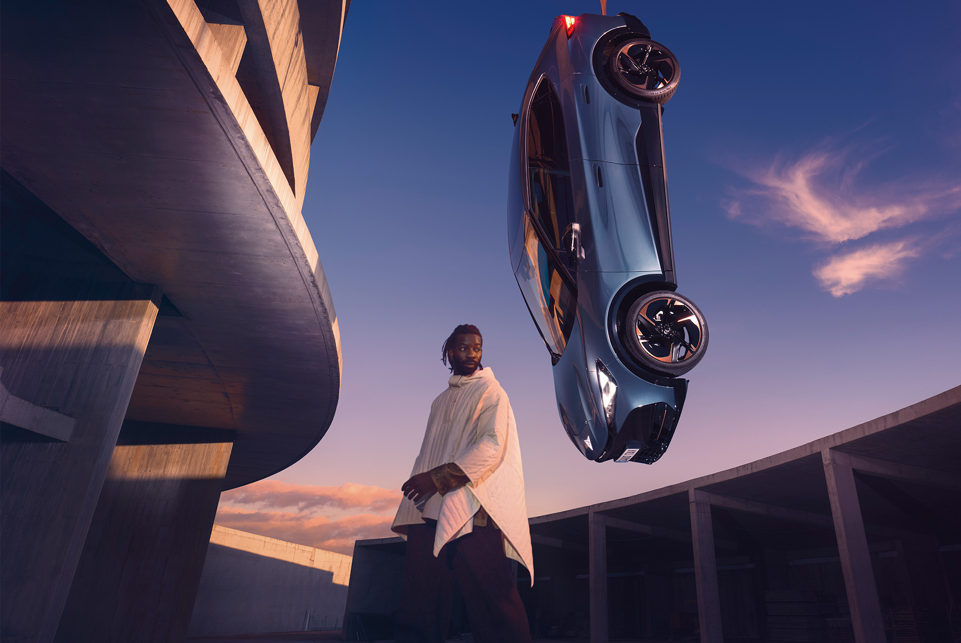 new cupra tavascan 2024 in blue with triangle eye headlights on and copper accent wheels, side shot, model in white clothing, suspended in air, cement structure and sunset